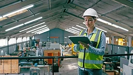 This image depicts a manufacturing engineer or worker using a tablet to update records within a factory setting. 