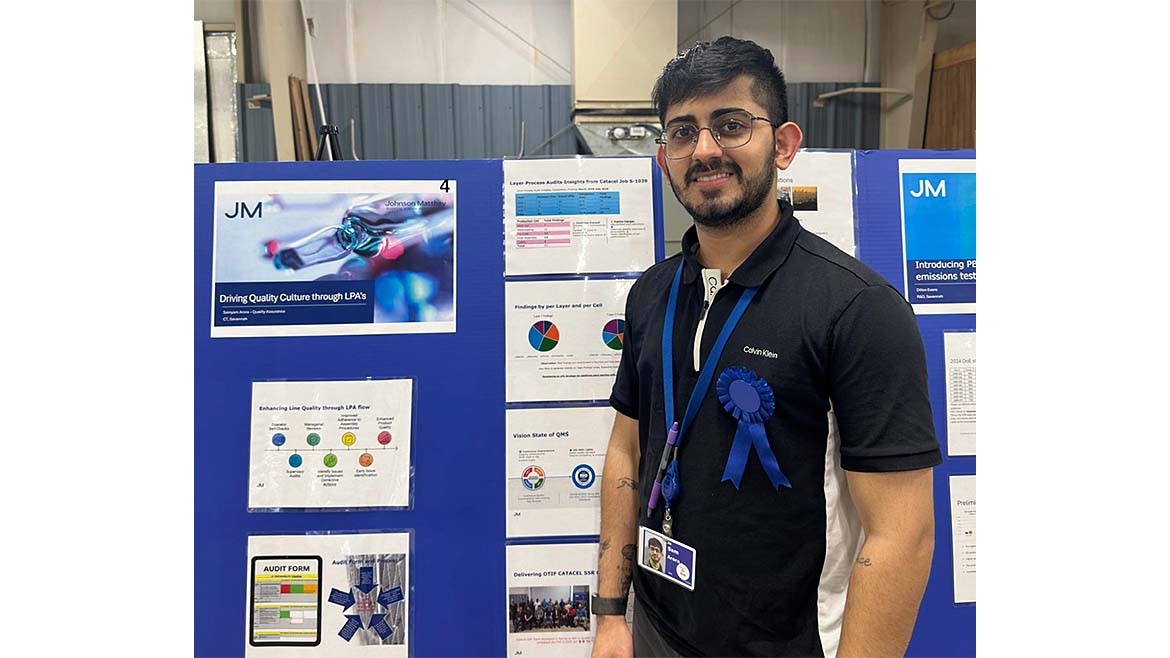 Arora standing in front of a blue display board featuring scientific or technical posters