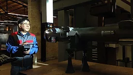 a person using a handheld device to interact with a large piece of industrial machinery or specialized equipment in a workshop setting.