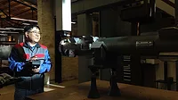 a person using a handheld device to interact with a large piece of industrial machinery or specialized equipment in a workshop setting.