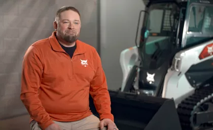 This image shows a person seated next to a Bobcat T66 compact track loader. This image shows a person seated next to a Bobcat T66 compact track loader.