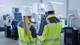 industrial professionals in safety gear discussing a process on a factory floor.