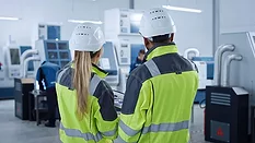 industrial professionals in safety gear discussing a process on a factory floor.