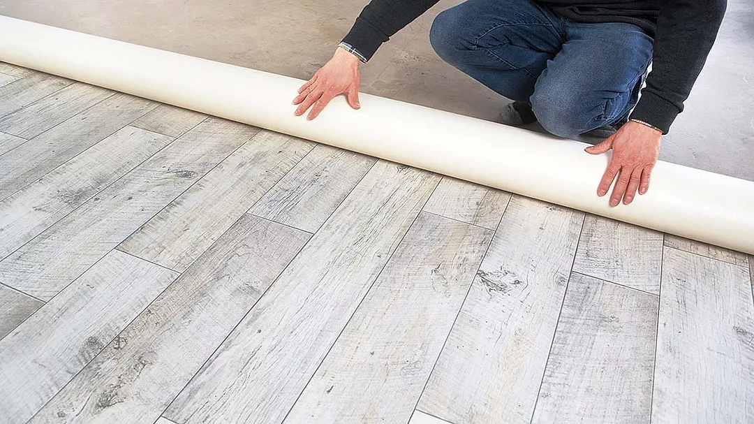 a person installing or rolling out sheet vinyl flooring