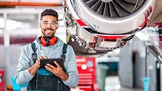 an aircraft technician smiling while using a digital tablet for maintenance tasks