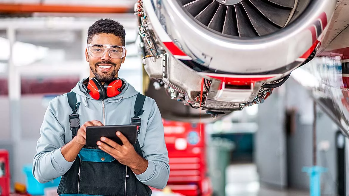an aircraft technician smiling while using a digital tablet for maintenance tasks