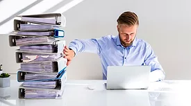 a person using a laptop while pushing away a large stack of office files