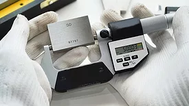 Gloved hands holding a handheld digital micrometer.